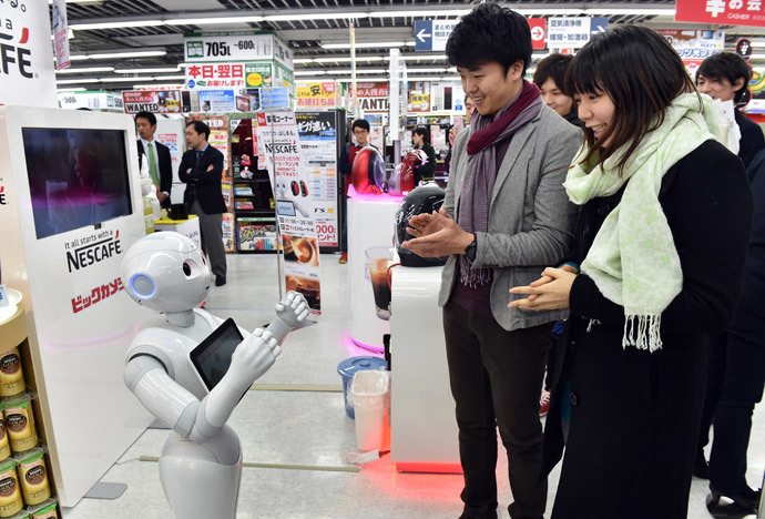 Japanese telecom giant Softbank's humanoid robot Pepper (L) attends to customers to introduce Nestle's coffee machines at an electric shop in Tokyo on December 1, 2014. (AFP Photo / Yoshikazu Tsuno)