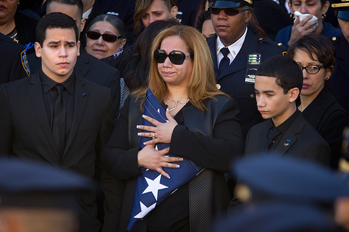 Justin Ramos (L) and Jaden Ramos ( R) flank their mother Maritza Ramos as she clutches a folded U.S. flag after the casket of their father, slain NYPD officer Rafael Ramos was loaded into a hearse at his funeral service at Christ Tabernacle Church to its final resting place in the Queens borough of New York December 27, 2014 (Reuters / Carlo Allegri)