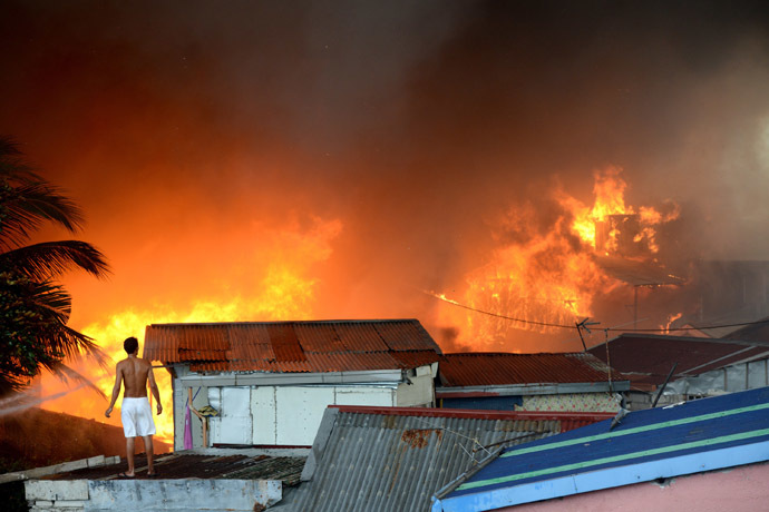 A man stands on a roof as he watches a fire engulfing a slum area in Manila on January 1, 2015. (AFP Photo)