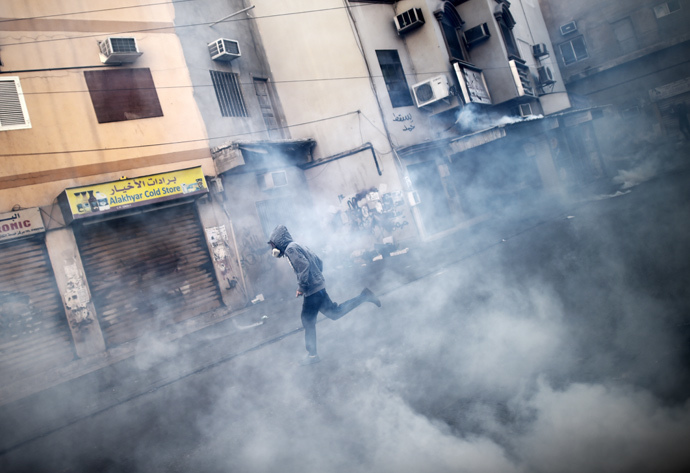 A Bahraini protestor runs for cover from tear gas during clashes with riot police following a protest against the arrest of the head of the banned Shiite opposition movement Al-Wefaq, Sheikh Ali Salman (on the poster) on January 1, 2015 in Bilad al-Qadeem, a suburb of Manama. (AFP Photo / Mohammed Al-Shaikh)