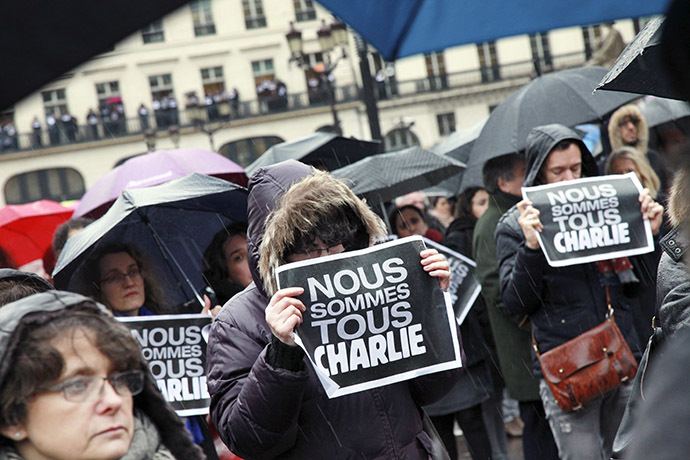 People hold signs reading "Nous sommes tous Charlie" (We are all Charlie) place de la Bourse in Paris as they observe a minute of silence on January 8, 2015. (AFP Photo/Loic Venance)