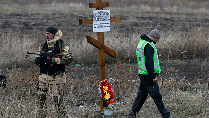 A member of the recovery team works at the site where the downed Malaysia Airlines flight MH17 crashed as an armed security representing the self-proclaimed Donetsk People's Republic stands guard near a cross erected by local residents in memory of victims (Reuters / Maxim Zmeyev)