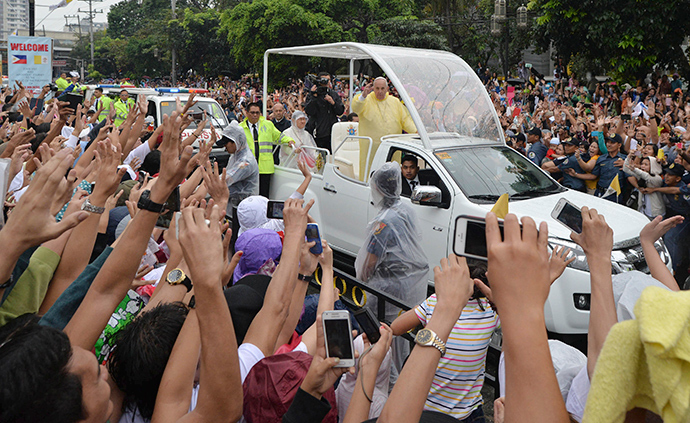 Pope Francis, wearing a raincoat, waves to well-wishers during a meeting with youths at the University of Santo Tomas (UST) in Manila January 18, 2015 (Reuters / Ezra Acayan)