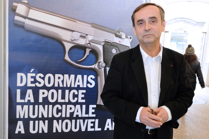 Beziers mayor Robert Menard poses on February 11, 2015 in front of a municipality campaign poster showing an automatic 7.65 handgun, with a campaign slogans reading : "From now on, the Municipal Police has a new friend". (AFP Photo / Sylvain Thomas)