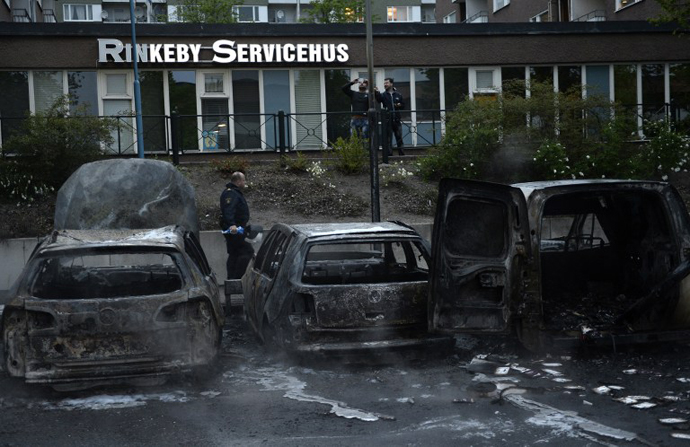 A police officers passes the scene of cars gutted by fire in the Stockholm suburb of Rinkeby after youths rioted in several different suburbs around Stockholm, Sweden for a fourth consecutive night on May 23, 2013. (AFP Photo / Jonathan Nackstrand)