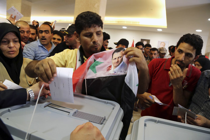 A Syrian national living in Beirut casts his vote ahead of the June 3 presidential election as he holds a Syrian national flag with Syria's President Bashar al-Assad's picture on it at the Syrian Embassy in Yarze, east of Beirut May 28, 2014. (Reuters)