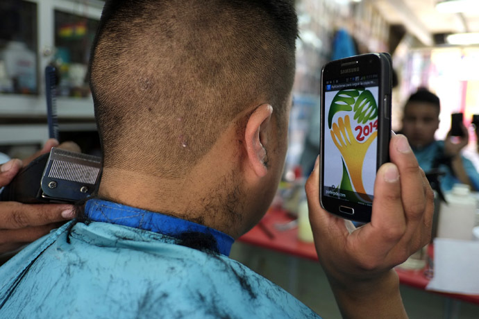 A soccer fan holds up his mobile phone showing the 2014 World Cup logo, which he is getting shaved on his head, at a hairdresser in La Paz, July 7, 2014. (Reuters/David Mercado)