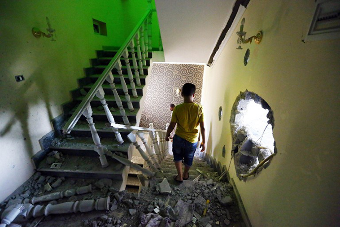 A youth walks down the stairs near a hole in the wall of a house at a former Libyan army camp known as Camp 27, in the Libyan capital Tripoli, on August 11, 2014 following reported clashes between rival militias. (AFP Photo / Mahmud Turkia)
