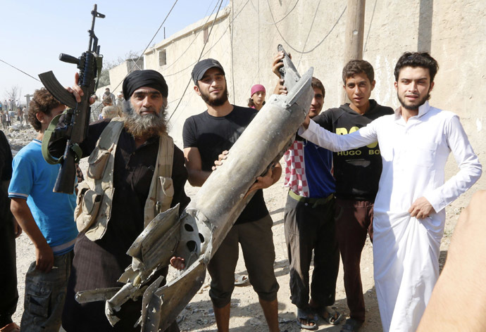 An Islamic State militant (L) stands next to residents as they hold pieces of wreckage from a Syrian war plane after it crashed in Raqqa, in northeast Syria September 16, 2014. (Reuters/Stringer)