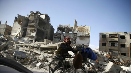 Un homme handicapé, en bicyclette, passe devant des bâtiments endommagés dans la ville assiégée de Douma, dans l'est de la Ghouta.