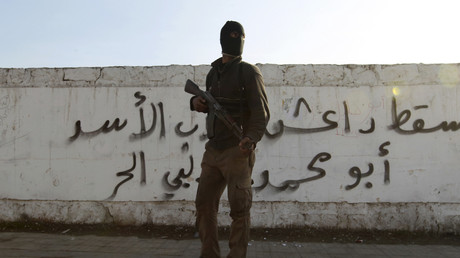 Un combattant de l'armée syrienne libre porte son arme devant un graffiti sur lequel on lit le mot Daesh, dans le quartier de Masaken Hanano à Alep le 7 janvier 2014.