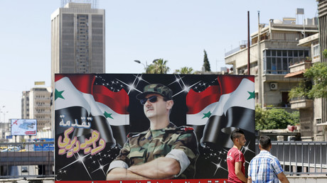 Deux Syriens passent devant un portrait de Bachar el-Assad à Damas, le 9 juillet
