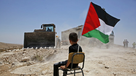 Un enfant assis et tenant le drapeau national palestinien assiste à la démolition par les autorités israéliennes d'un site scolaire dans le village de Yatta, au sud de la ville d'Hébron, en Cisjordanie, le 11 juillet 2018.