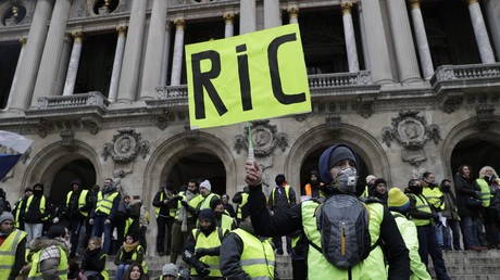Un manifestant des Gilets jaunestient un carton pancarte portant l'inscription Référendum d'initiative citoyenne (RIC) devant l'opéra devant Paris, lors de l'acte V de la mobilisation des Gilets jaunes, le 15 décembre 2018.