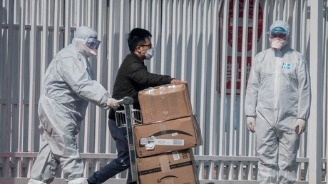 Des travailleurs portant des combinaisons de protection à titre préventif contre le coronavirus COVID-19 aident un passager à transporter ses affaires au New China International Exhibition Center, à Pékin, le 16 mars 2020 (image d'illustration).