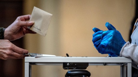 Un électeur dépose son bulletin devant un fonctionnaire équipé de gants en plastique dans un bureau de vote de Lyon, le 15 mars 2020, lors du premier tour des élections municipales.