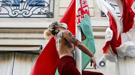 Une activiste du mouvement Femen ajoute au drapeau national biélorusse le drapeau blanc et rouge utilisé par les manifestants biélorusses, au mât se trouvant dans l'enceinte de l'ambassade de Biélorussie à Paris, le 11 septembre 2020.
