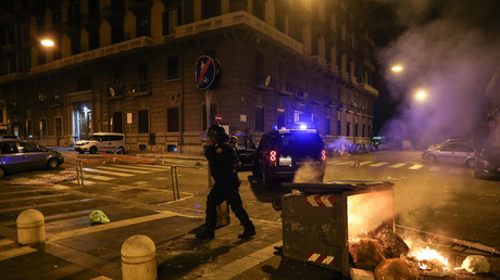 Un policier anti-émeute italien passe devant une poubelle en feu dans le centre ville de Naples, le 23 octobre 2020.