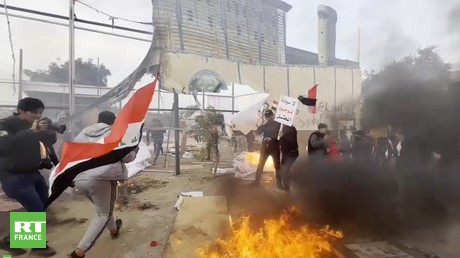 Des manifestants brandissent le drapeau irakien devant la réplique endommagée de l'ambassade américaine à Bagdad, en Irak, le 31 décembre 2021.