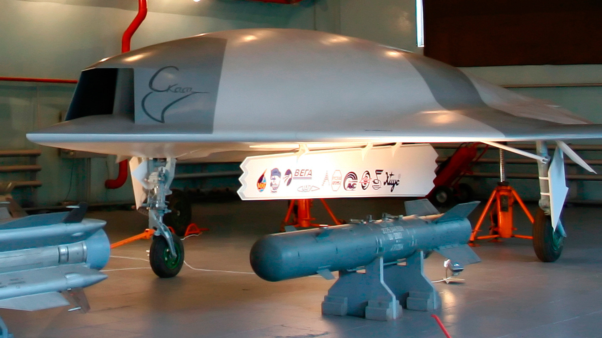 Modelo em tamanho real do veículo aéreo não tripulado Skat (ao fundo) e bombas aéreas (em primeiro plano) em um hangar da fábrica de aeronaves MiG