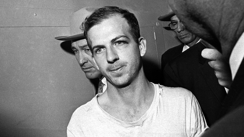 Lee Harvey Oswald is led down a corridor of the Dallas police station