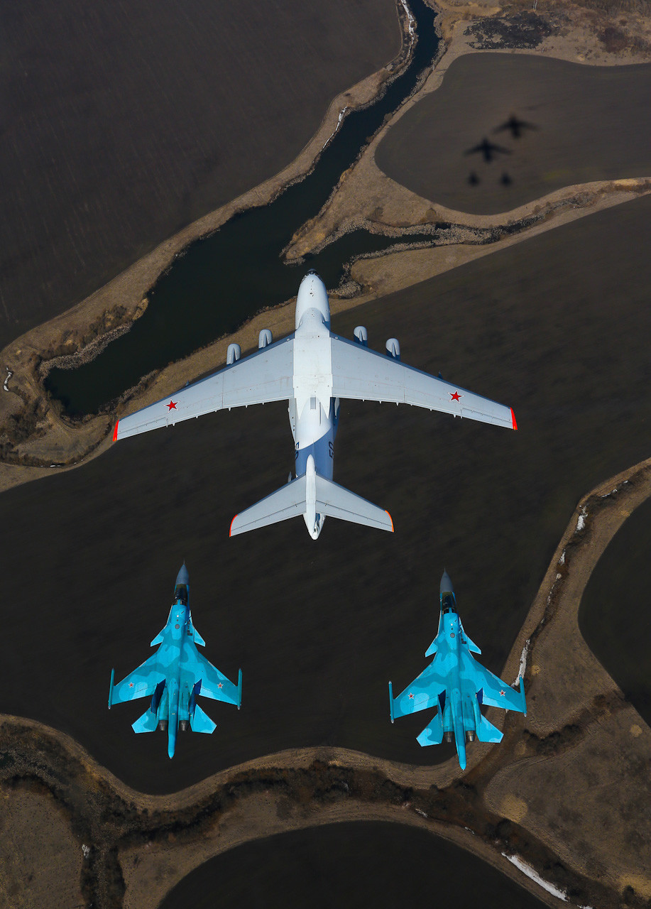 Avião para reabastecimento em voo quadrimotor Ilyushin Il-78 (baseado em seu irmão Il-76), acompanhado de dois caças-bombardeiros russos de dois assentos Su-34