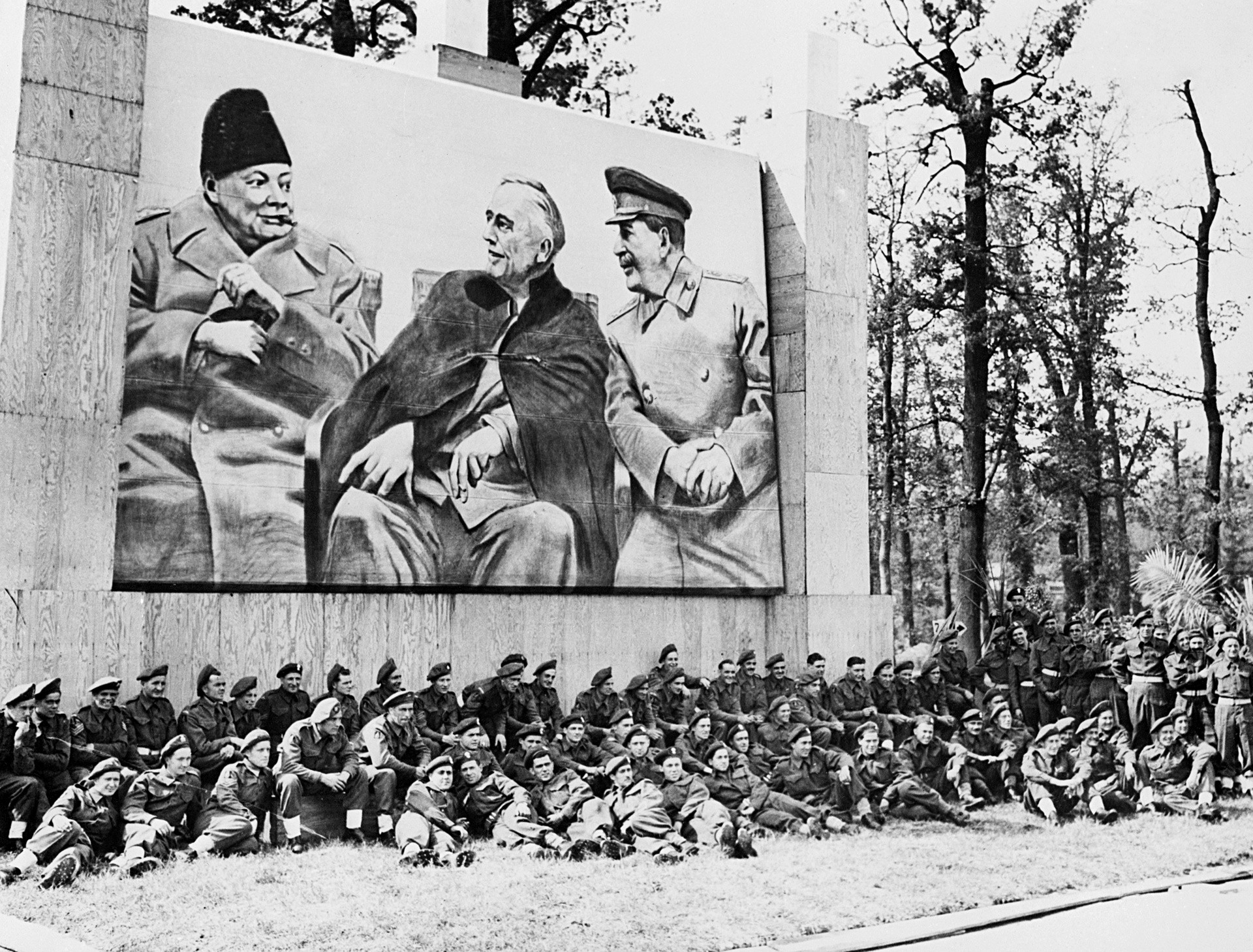 Британски војници, учесници Параде победе савезника у Берлину, одмарају се испод великог плаката са портретима Черчила, Рузвелта и Стаљина у Јалти. 
