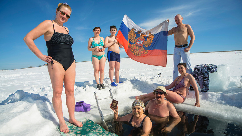Russian winter swimming enthusiast pose for a photo, displaying a Russian national flag as they celebrate on the day of the Russian presidential election day in Novosibirsk, Russia.