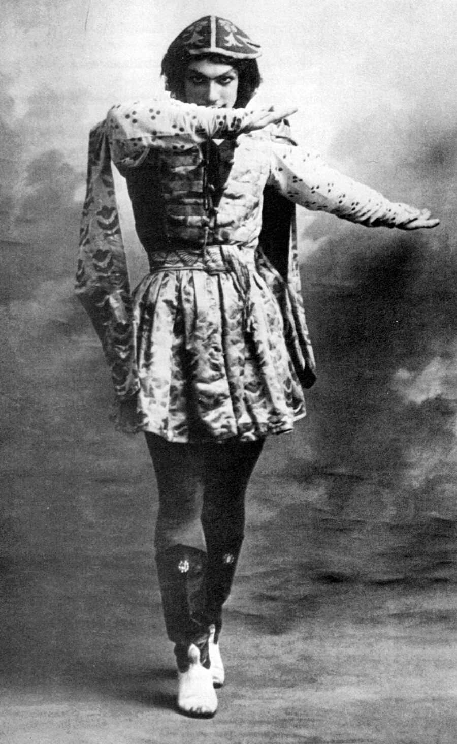 Vaslav Nijinsky (1889-1950) was a Russian ballet dancer who is often cited as the greatest male dancer of the early 20th century. Here he is wearing high boots and a long tunic, peering above his right arm, left arm extended to the side in the Grand pas classique hongrois from Le festin.