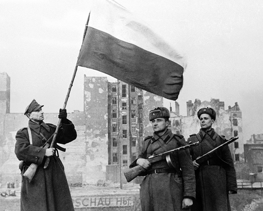 Poljski vojak (levo) in sovjetska vojaka dvigujejo zastavo nad osvobojeno Varšavo, 17. januar 1945.