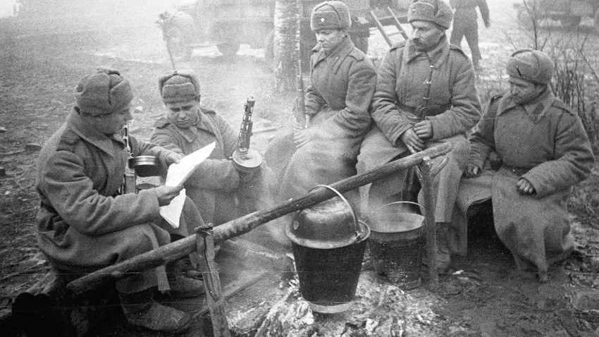 Soviet soldiers cooking food, reading a paper and warming themselves at the fire
