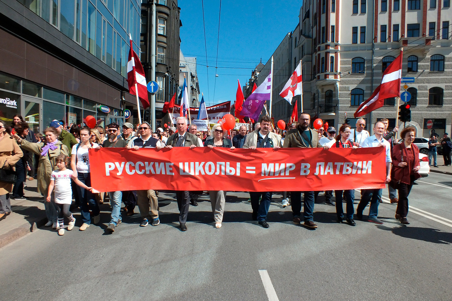 Masyarakat berunjuk rasa selama Hari Buruh Internasional, 1 Mei 2018, di Riga, ibu kota Latvia, menentang penggunaan penuh bahasa Latvia dalam pendidikan formal dan “optimalisasi” sekolah.