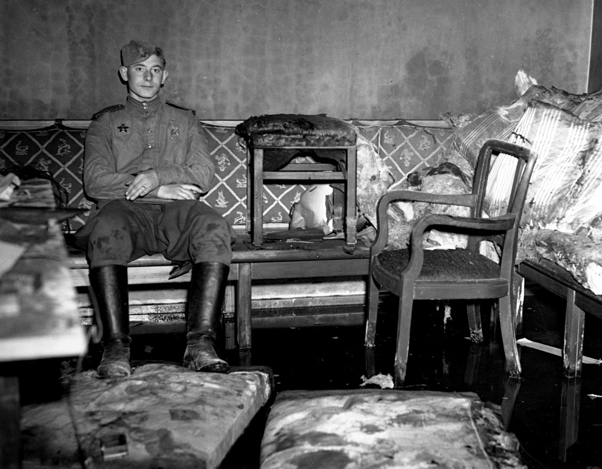A Russian soldier sitting on the sofa upon which German dictator Adolf Hitler is reported to have killed himself,