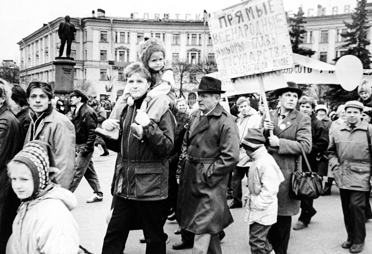 Esta foto mostra Aleksandr Chmonov (carregando um cartaz) no primeiro semestre de 1990, durante campanha eleitoral no subúrbio de Kolpino, em Leningrado.