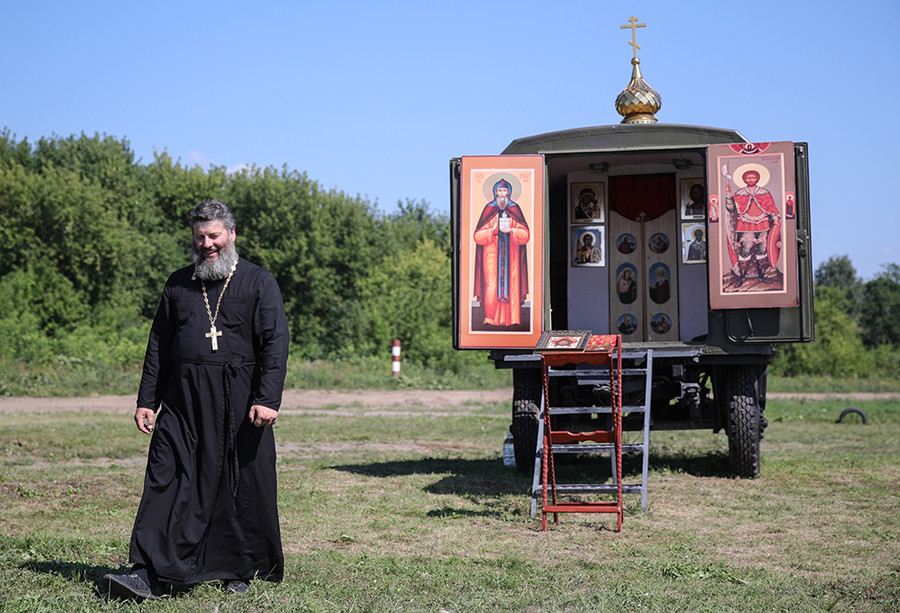 A Russian Orthodox priest near a mobile chapel, during the Open Water contest between pontoon bridge units at the 2018 International Army Games.