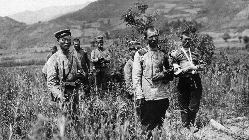 日露戦争（1904ー1905）、満州、中国。日本の兵士たちが負傷したロシア帝国の兵士を仮包帯所ヘ連れて行く。