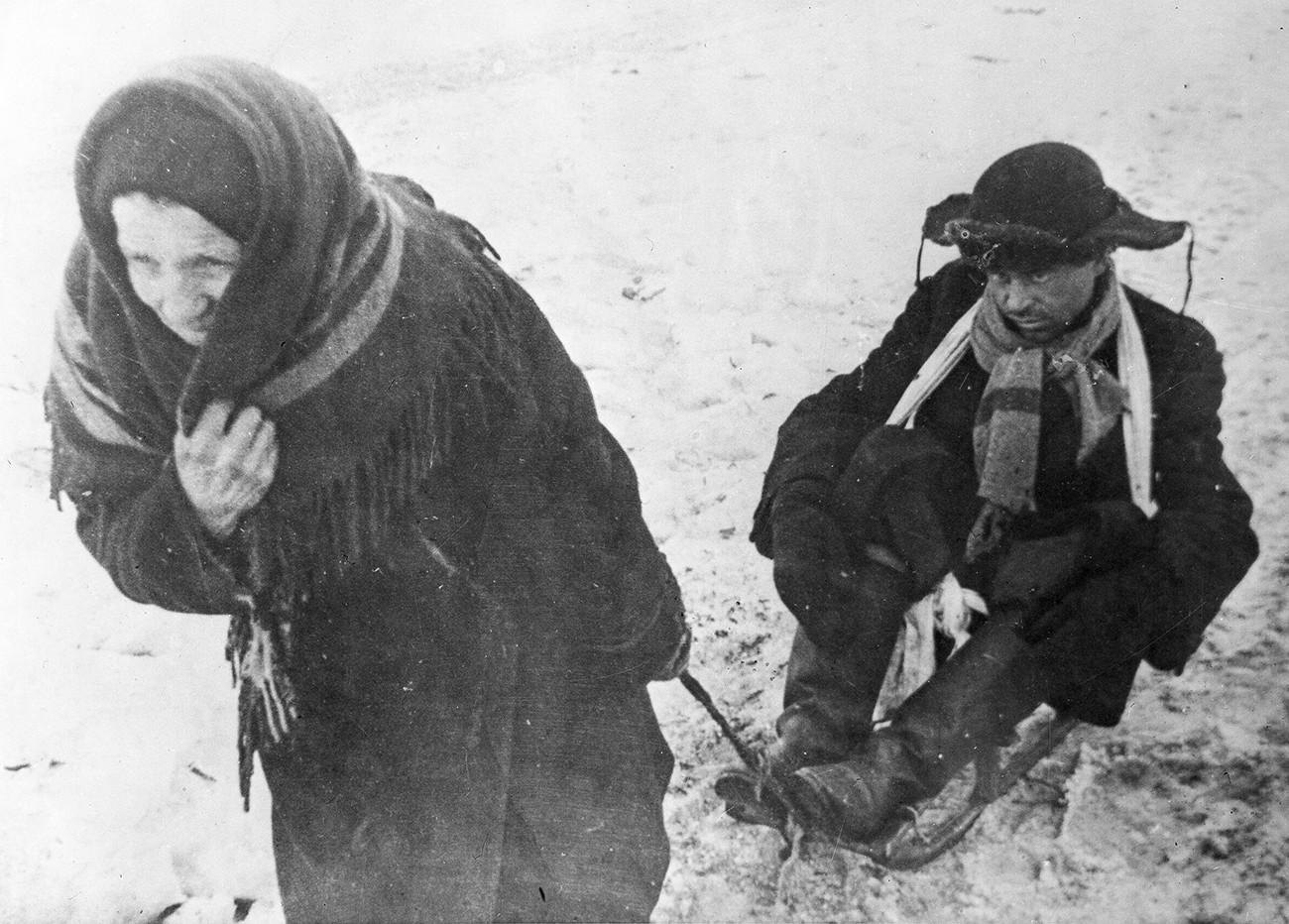 Seorang wanita menarik kereta luncur yang membawa suaminya yang kekurangan gizi, di Leningrad, selama Pengepungan.