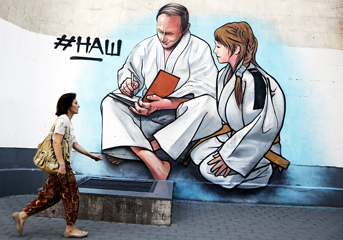 Mujer pasea frente a un grafiti de Putin, representado con un kimono de judo, en la ciudad crimea de Yalta.