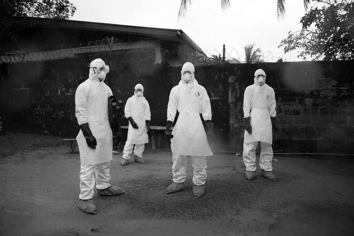 Tim za uklanjanje tijela čeka da se kuća poprska klorom prije nego što uđu da bi uklonili tijelo koje je ubila ebola.

