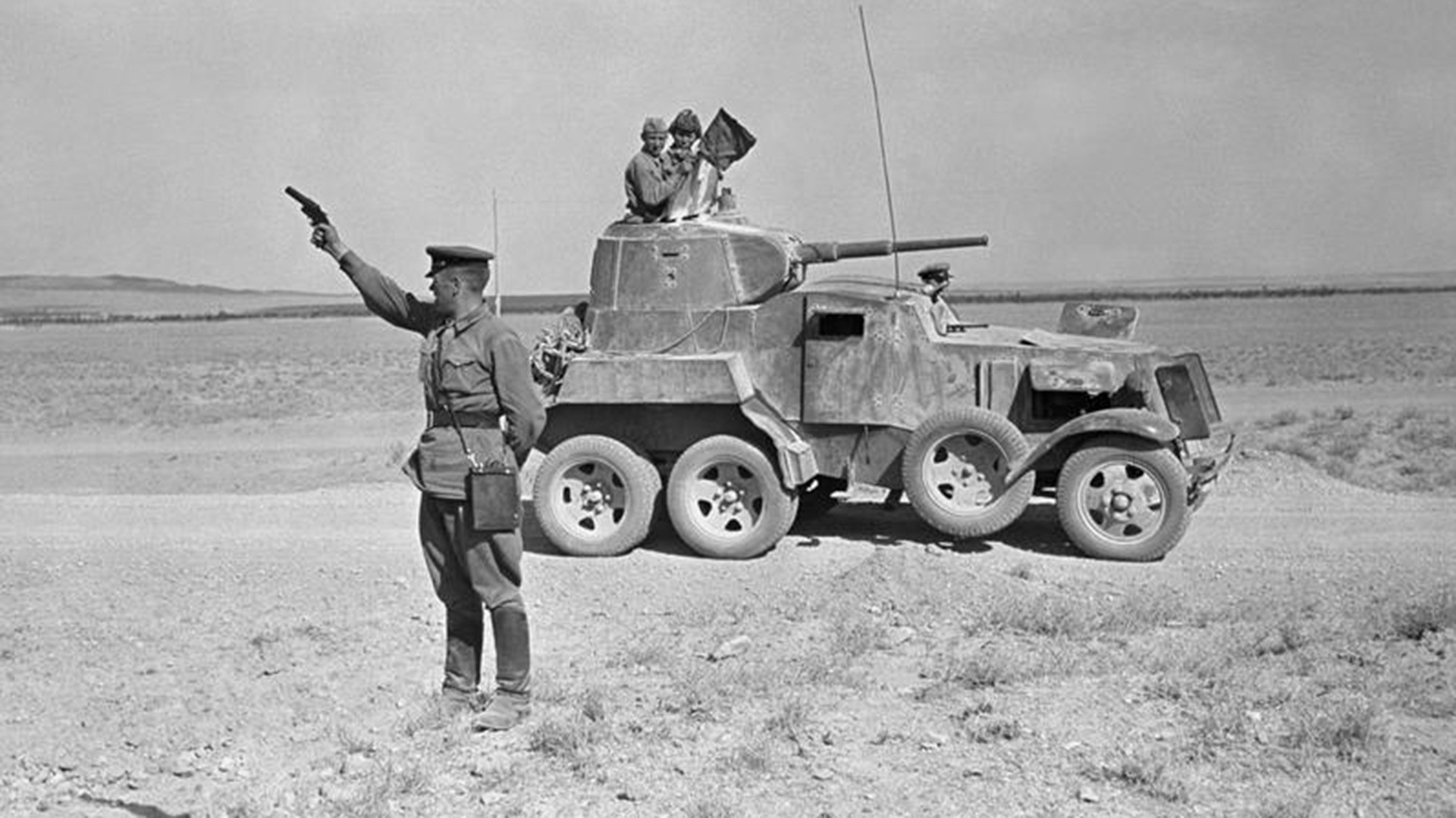 Sovjetski časnik puca iz signalnog pištolja negdje u iranskoj pustinji. Iza njega je oklopno vozilo BA-10.