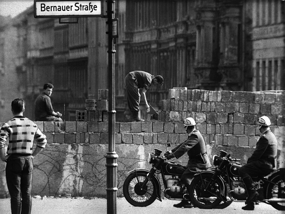 Police officers on a motorbike watch workers lay bricks on the other side of the so-called Berlin Wall in the street Bernauer Strasse in Berlin, Germany. On the morning of August 13, 1961,