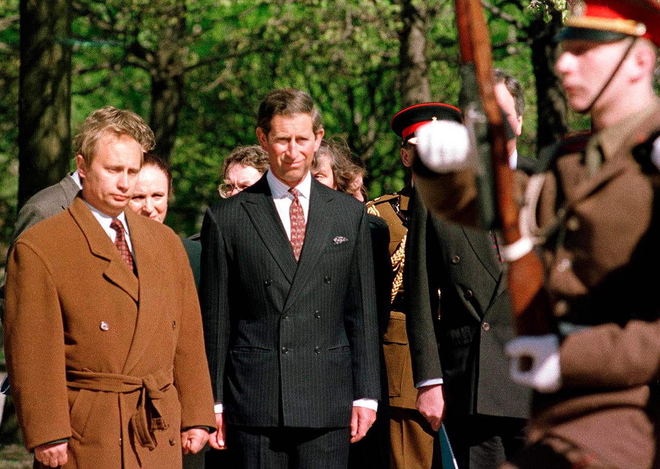 Владимир Путин (лево), који је тада био задужен за спољне односе Санкт Петербурга код градоначелника Анатолија Сопчака, присуствује церемонији полагања венца са принцом  Чарлсом на Пискарјовском гробљу у Санкт Петербургу. Фотографија начињена 17. маја 1994. године