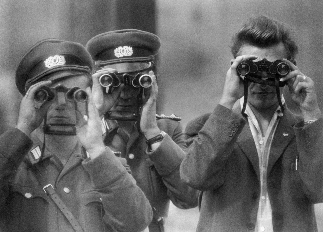 Due poliziotti della Germania dell'Est e un civile guardano con il binocolo la costruzione del Muro di Berlino
