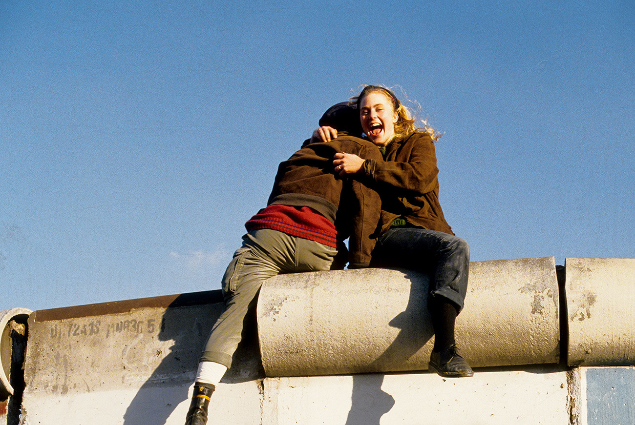 Pasangan kekasih berpelukan di atas Tembok Berlin merayakan keruntuhan tembok itu.
