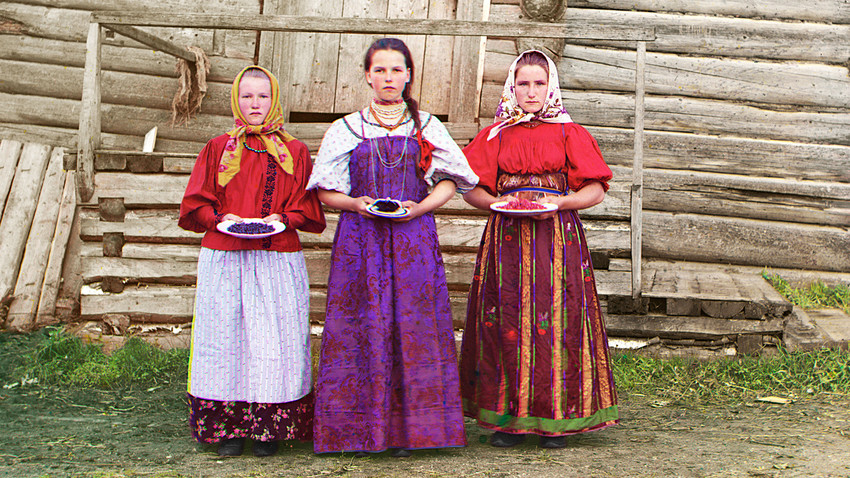 Young Russian peasant women in front of traditional wooden house, in a rural area along the Sheksna River near the small town of Kirillov. Early color photograph from Russia, created by Sergei Prokudin-Gorsky as part of his work to document the Russian Empire from 1909 to 1915.