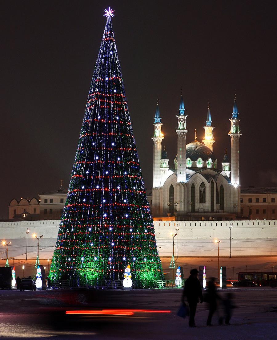 People pass by a New Year's tree, with the Kul Sharif Mosque in the background, in the Russian city of Kazan.