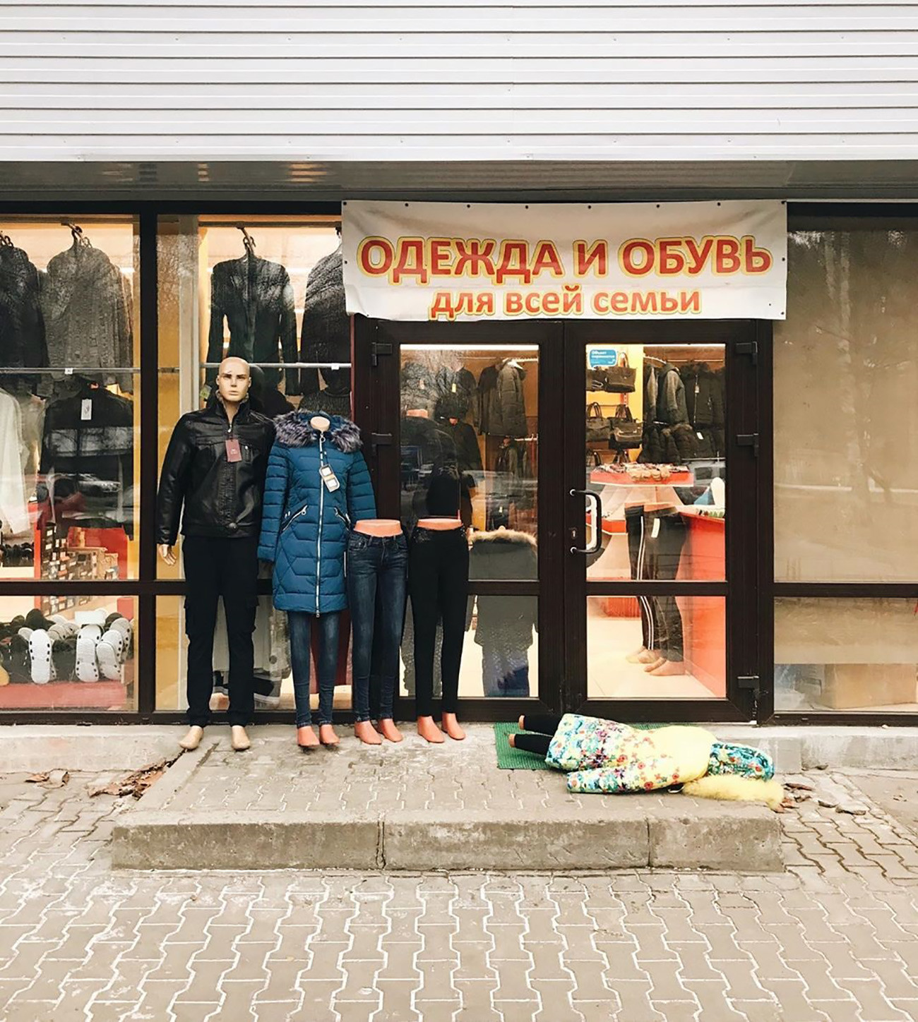 看板に書かれている文字「家族みんなのための衣服と靴」。キャプション：「家族は堂々と強くあるためのルーツを与えてくれる　© Larisa Guzeyeva」。
