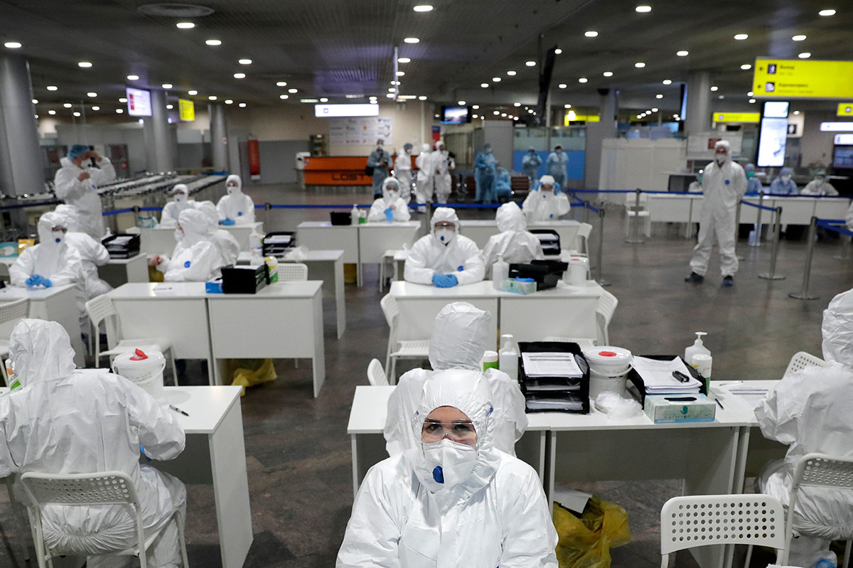 Especialistas médicos russos aguardam passageiros que chegam de países estrangeiros para teste no aeroporto Sheremetievo, em Moscou 
