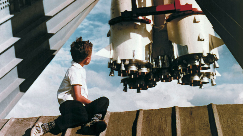 Млади посетилац Изложбе достигнућа народне привреде СССР-а седи на платформи испред ракете „Восток“ близу павиљона „Космос“.