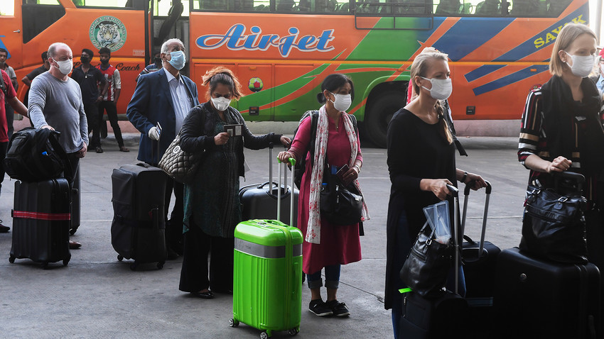Extranjeros con máscaras medicas se alinean fuera de la terminal de salida del Aeropuerto Internacional Subhash Chandra Bose de Netaji para abordar un vuelo especial de evacuación